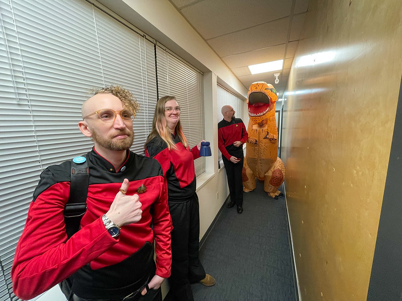 Max, Cori, Ian, and Andrew wait in the hallway outside the main studio. Everyone is in a red Star Trek TNG command uniform except for Andrew, who is wearing an inflatable t-rex costume. Max is giving the thumbs up sign in the foreground.