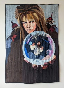 A quilted version of a Labyrinth movie poster. David Bowie as the Goblin King holds a crystal ball with protagonist Sarah inside, arms wide and looking for a way out.