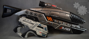 Two Mass Effect guns positioned side by side. One is a long black assault rifle (M8 Avenger) and the other is a short gray pistol (M77 Paladin).