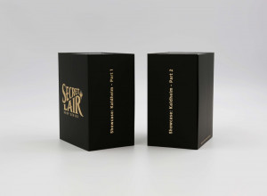 Two black boxes stand on their ends. The words "Secret Lair" are embossed on the front in gold, while the sides of each deck read "Showcase Kaldeim" Part 1 and Part 2.