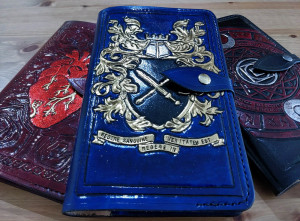 Three hand-tooled leather notebooks elaborately decorated with detail work and the symbol of a heart, a pair of crossed swords, and an arcane hex.