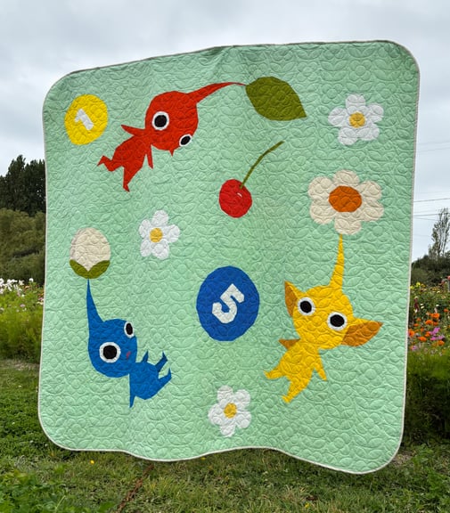 The same quilt, in hanging outside in front of a flower field to help show the scale of the quilt.