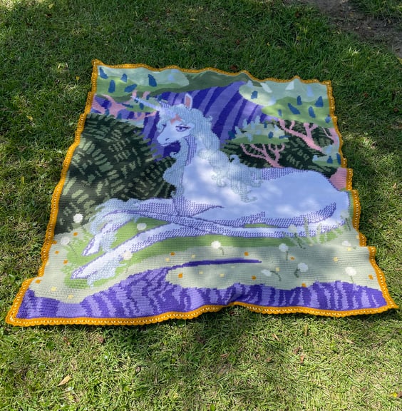 The dappled sunlight and grassy background in this image are warm and inviting and really bring out the whimsical nature of the blanket and The Unicorn herself. The border of the blanket is fully visible here and is meant to evoke an elegant but understated frame. 