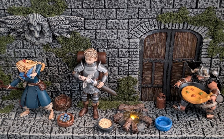 Another close-up of several characters, giving a better shot of the campfire. Marcille and Laios sit to the left of the campfire, while Senshi carries a large pan full of yellow-ish stew to the fire. The campfire is lit with a glowing golden LED.