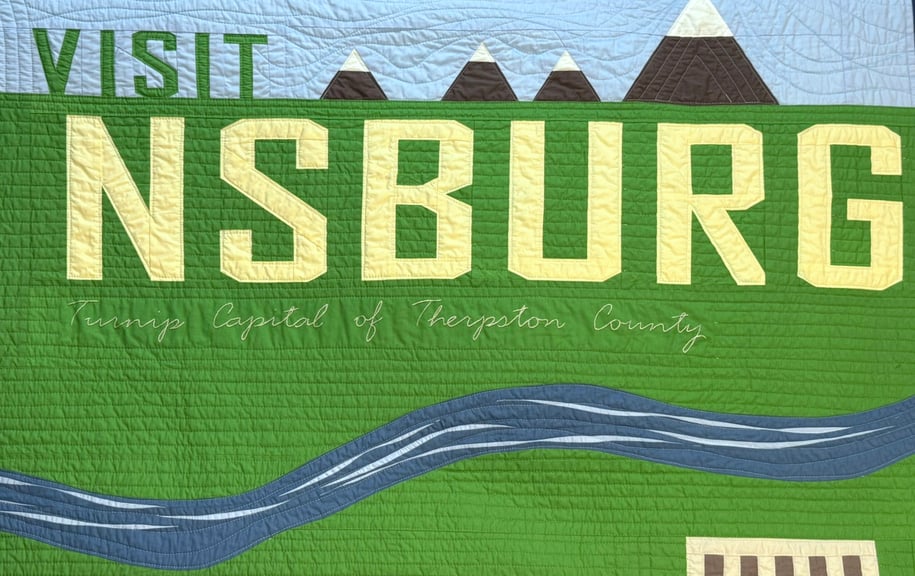 A close-up on the quilt reading "Visit Nsburg - Turnip Capital of Therpston County"