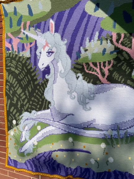 This is a closer look displaying some of the detail of the piece and illustrating its versatility. It is hung against the brickwork of the house to show off that while it is a cozy addition to the blanket pile, it can be used as a wall hanging as well.