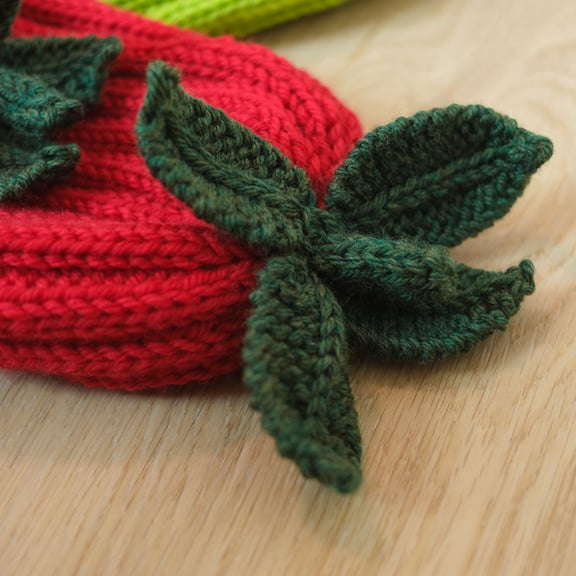 A close up of the knitted leaf and stem applique on the top of a red knitted hat.