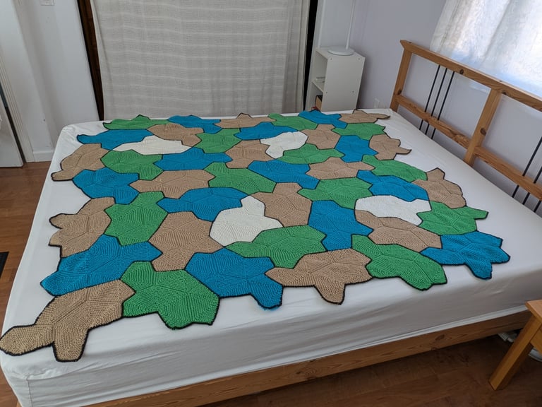 The same blanket, this time on a queen-sized bed with no pillows. The blanket mostly covers the bed, but it is not large enough to hang off the sides or foot of the bed.