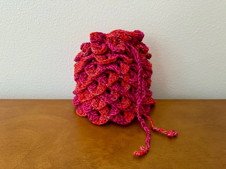 Alpha Flight themed dice bag, crocheted from a cotton blend yarn with metallic strand. Measures 7.5" tall x 7" wide
