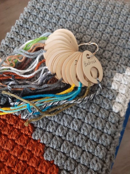 A series of wooden chips, labeled with block names, each one has a length of yarn attached to show which yarn was used for which block, serving as a legend for the scarf. Fun fact, this wall had no lapis, copper, or redstone blocks, so they are not included.