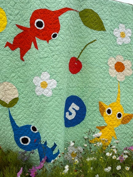 A close up of the all three Pikimin that make up the central motif of the quilt with some white and purple flowers in front.