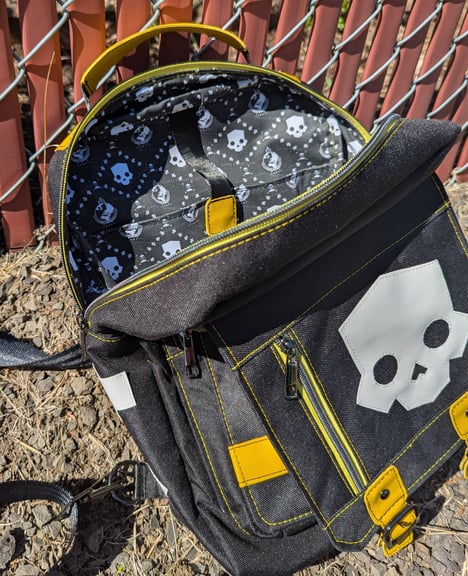 An open black canvas backpack with yellow vinyl accents, the main zipper compartment is pulled open to show off the interior fabric.