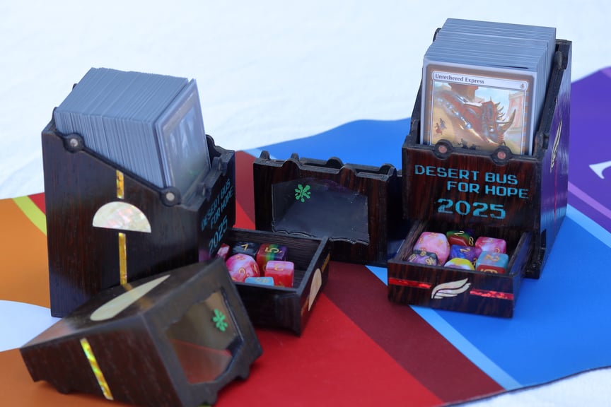 A closer view of the Dawn Guard and Alpha Flight boxes, now sitting open. The lids are removed and sitting on the playmat beside the boxes, showing green bug splats on the otherwise clear windows. The drawers are also open, showing that each one is full of colorful dice.