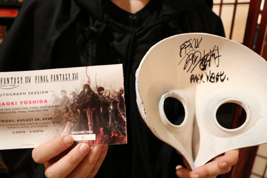 A photograph of the signing ticket for Yoshi P, as well as the inside of a white bird like mask from Final Fantasy 14, signed by Naoki Yoshida.
